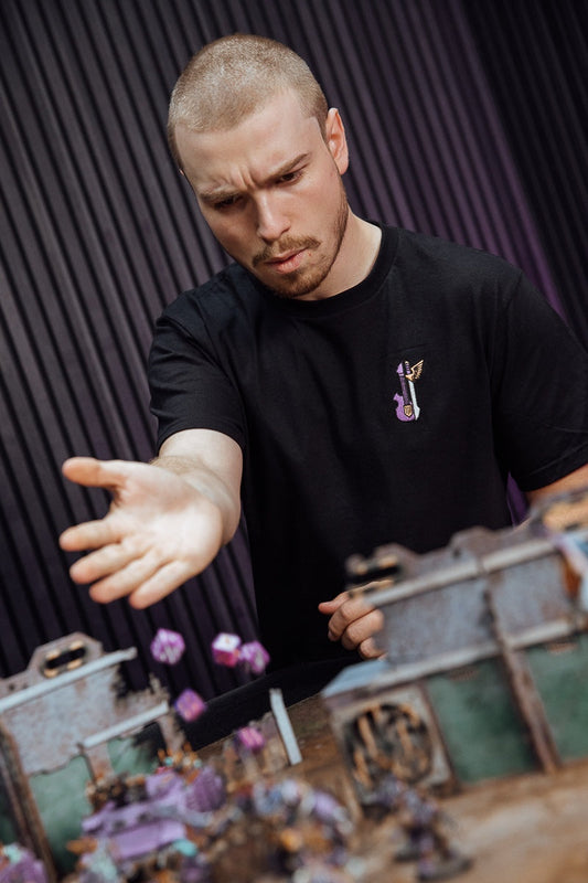 Tabletop wargamer rolling dice while wearing an embroidered gaming T-shirt